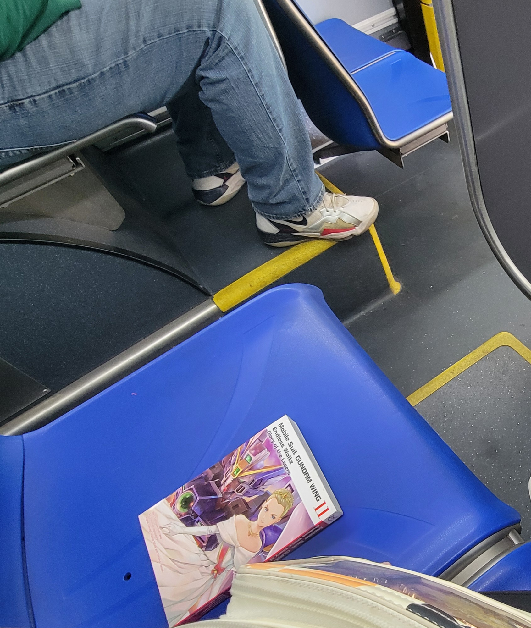 Gundam Wing Glory of Losers volume 11 with Relena in her queen of the world outfit on the cover on a plastic bus seat with a cat fanny in view.